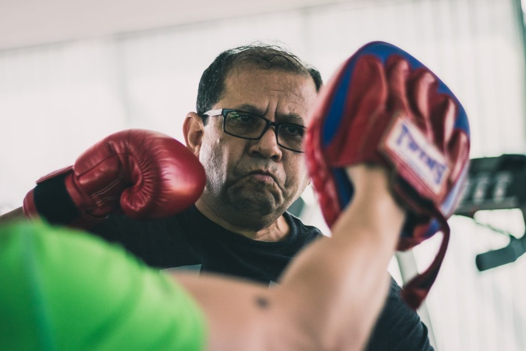 A senior/ older man doing boxing training guided by personal trainer in Singapore